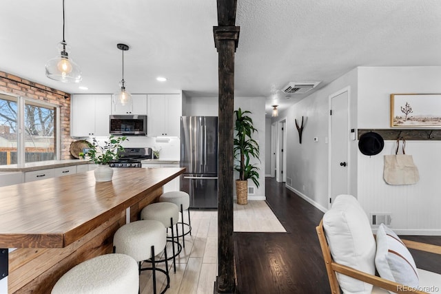 dining space with baseboards, visible vents, light wood-style flooring, and a textured ceiling