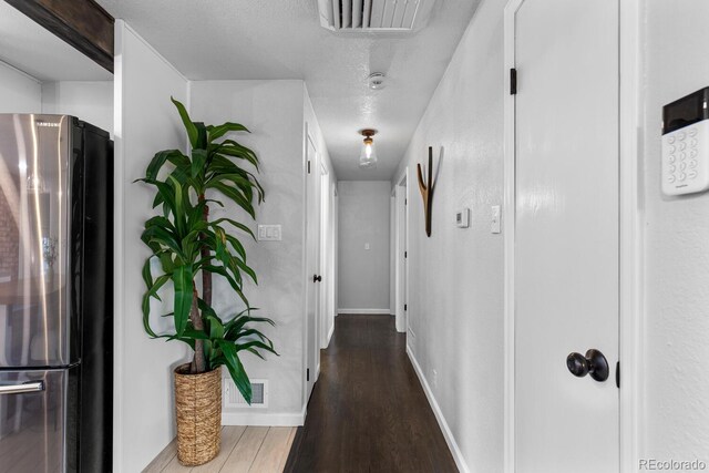 hallway featuring baseboards, a textured ceiling, visible vents, and wood finished floors