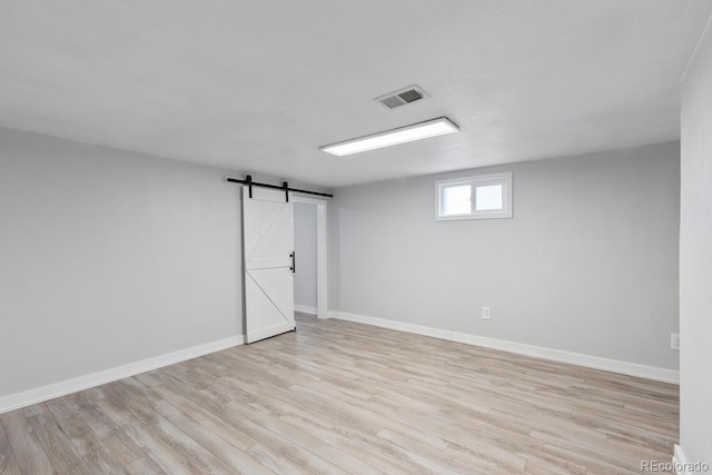 below grade area featuring light wood-style floors, visible vents, baseboards, and a barn door