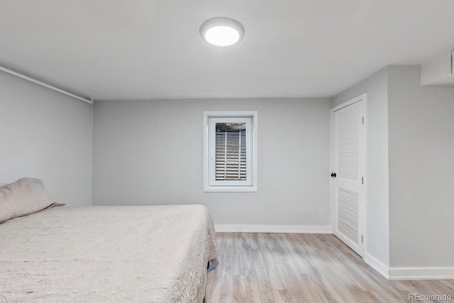 unfurnished bedroom featuring light wood finished floors, baseboards, and a closet