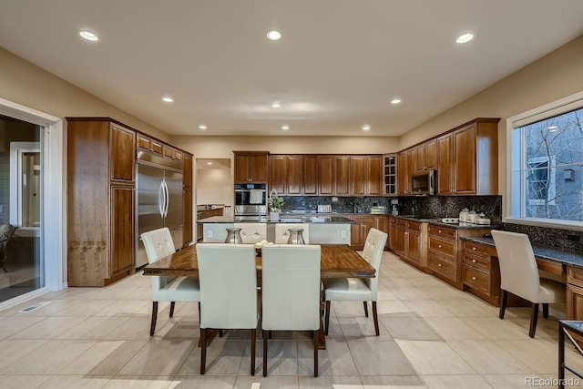 kitchen with stainless steel appliances, dark countertops, decorative backsplash, and an island with sink