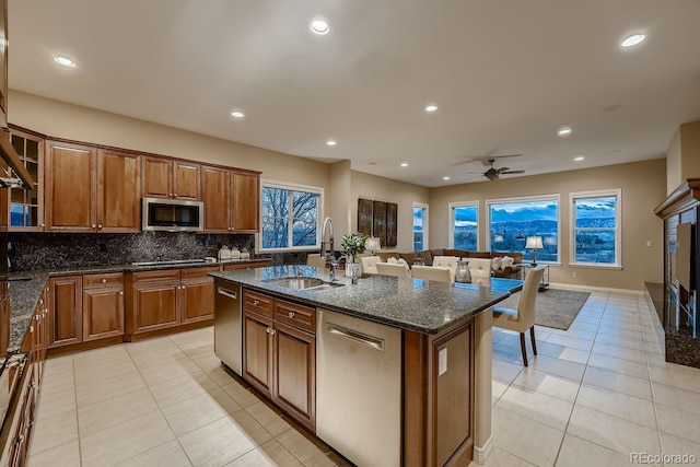 kitchen featuring light tile patterned floors, decorative backsplash, appliances with stainless steel finishes, brown cabinets, and a sink