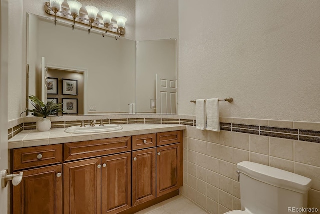 bathroom with toilet, tile patterned flooring, vanity, and tile walls