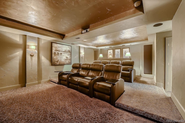 carpeted home theater featuring a raised ceiling, a textured wall, and baseboards