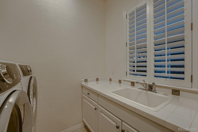 clothes washing area featuring cabinet space, baseboards, a sink, and washing machine and clothes dryer