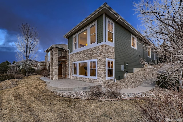 rear view of property featuring stone siding, a patio area, and a balcony