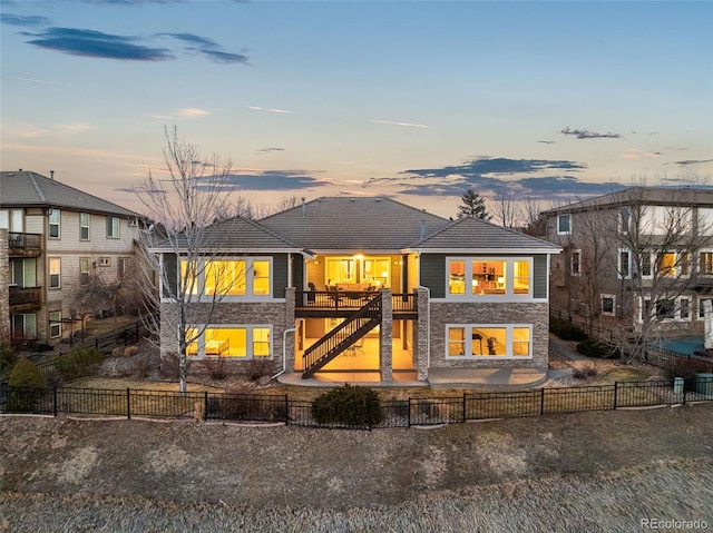 back of property at dusk with stone siding, a fenced backyard, stairway, and a patio