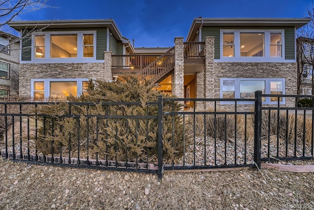 view of front of home featuring fence private yard, stone siding, and a balcony