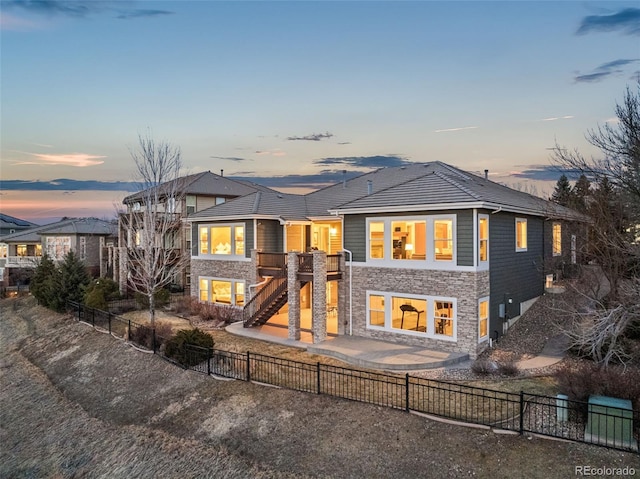 view of front of home with stone siding, a fenced backyard, a patio area, and stairs