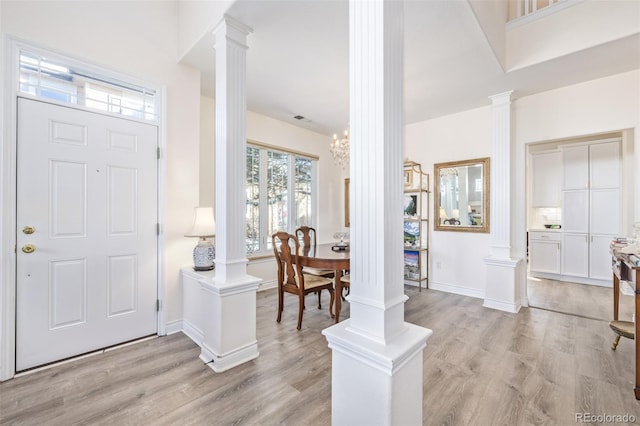 foyer with light hardwood / wood-style floors, a notable chandelier, and ornate columns