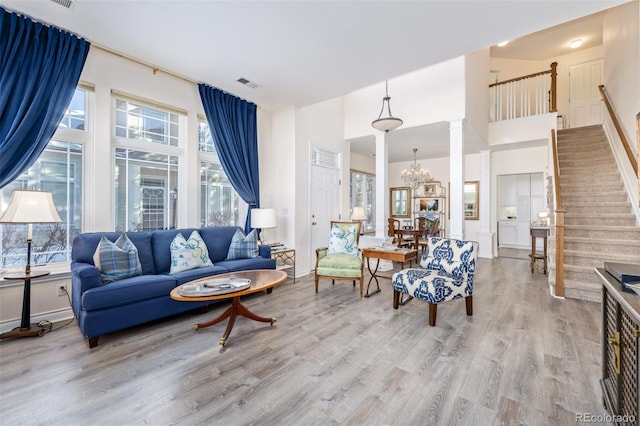 living room featuring decorative columns, light wood-type flooring, plenty of natural light, and an inviting chandelier