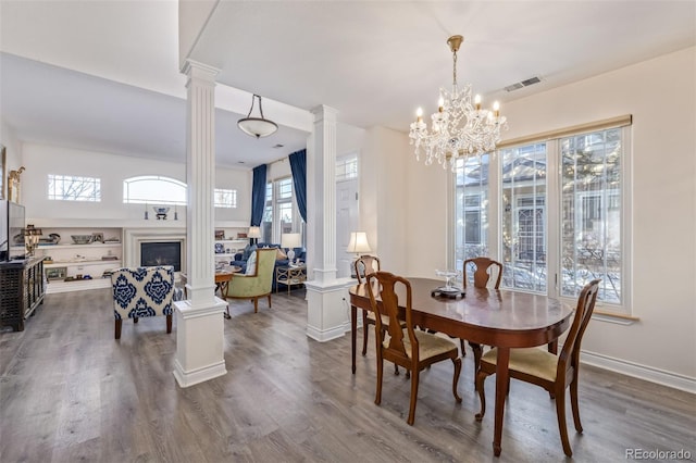 dining space with hardwood / wood-style floors, decorative columns, and a notable chandelier