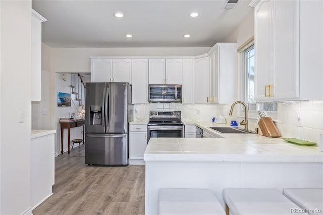 kitchen featuring appliances with stainless steel finishes, white cabinetry, sink, kitchen peninsula, and light hardwood / wood-style flooring