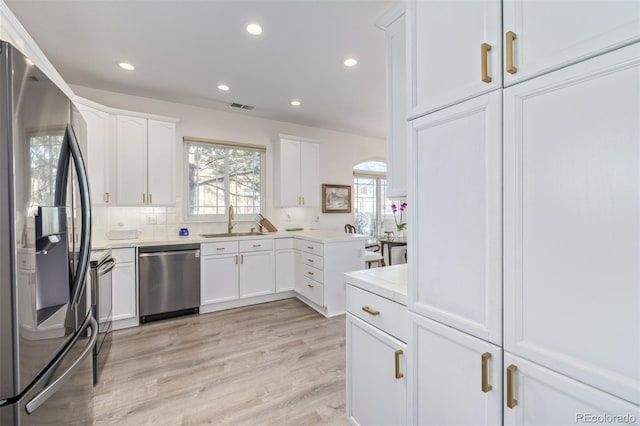 kitchen with white cabinets, appliances with stainless steel finishes, tasteful backsplash, light hardwood / wood-style floors, and sink