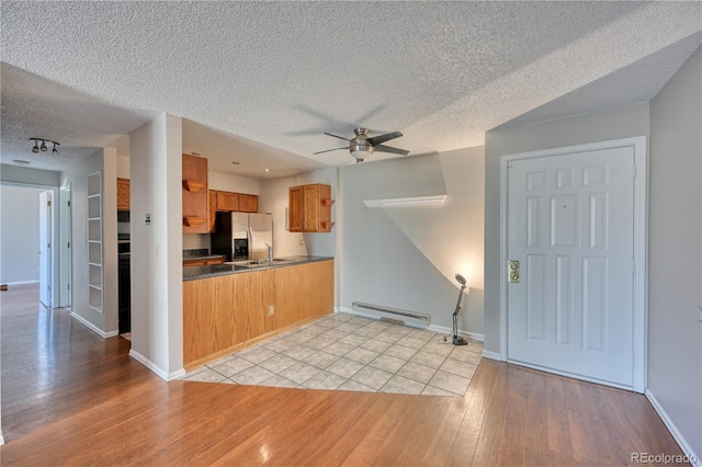 kitchen with a baseboard heating unit, stainless steel fridge with ice dispenser, brown cabinetry, light wood-type flooring, and a textured ceiling