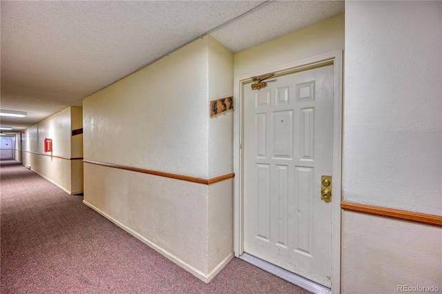 hall featuring carpet, a textured wall, a textured ceiling, and baseboards
