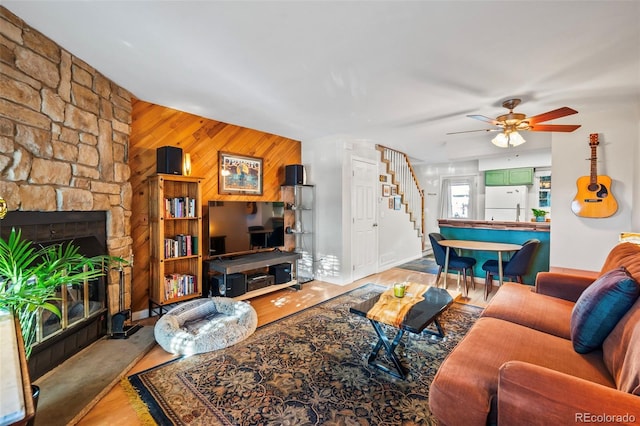 living room with a stone fireplace, wood walls, and ceiling fan