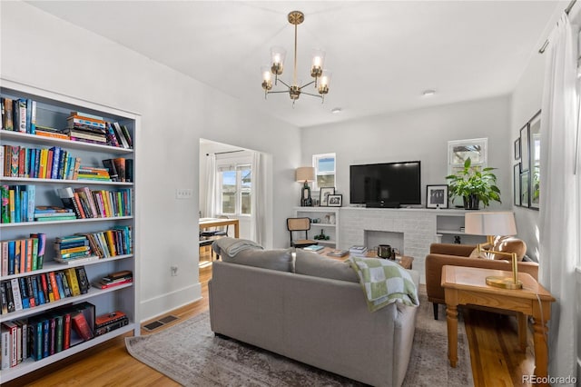 living room featuring an inviting chandelier, hardwood / wood-style floors, and a brick fireplace