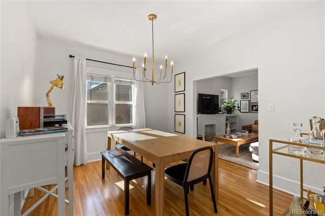 dining space with an inviting chandelier, a brick fireplace, and light hardwood / wood-style floors