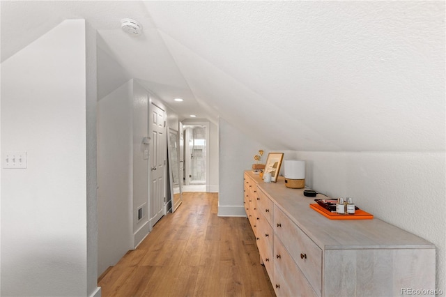 hall with lofted ceiling and light wood-type flooring