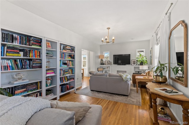 living room with an inviting chandelier, a brick fireplace, plenty of natural light, and light hardwood / wood-style floors