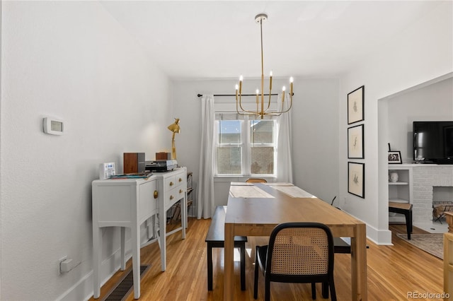 dining room featuring a notable chandelier, a fireplace, and light wood-type flooring