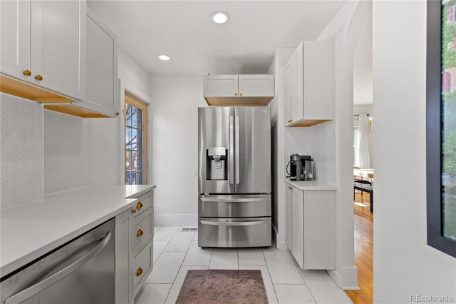 kitchen with stainless steel appliances, tasteful backsplash, light tile patterned floors, and white cabinets