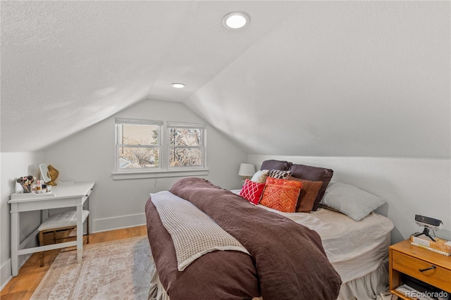 bedroom with lofted ceiling, a textured ceiling, and light hardwood / wood-style floors