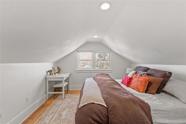 bedroom with vaulted ceiling, light hardwood / wood-style flooring, and a textured ceiling