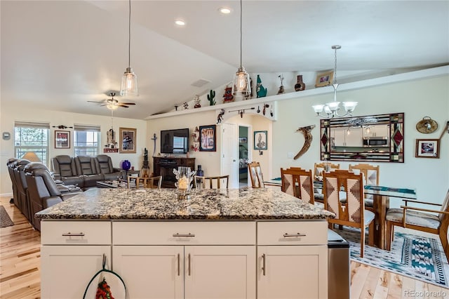 kitchen featuring white cabinets, ceiling fan with notable chandelier, hanging light fixtures, light hardwood / wood-style flooring, and dark stone countertops