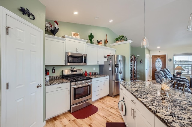 kitchen featuring lofted ceiling, dark stone counters, hanging light fixtures, white cabinetry, and stainless steel appliances