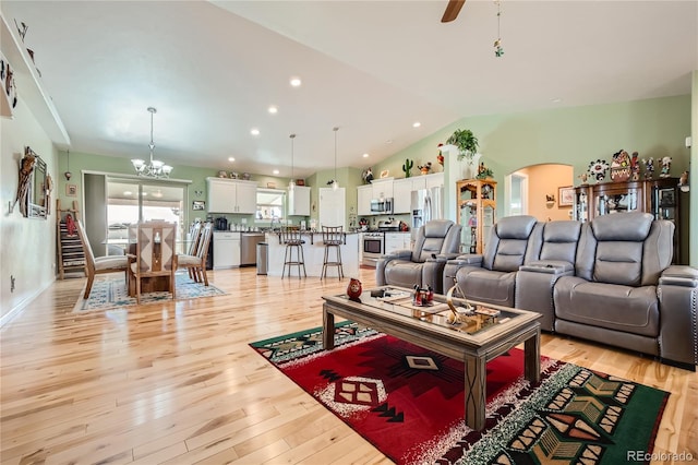 living room featuring lofted ceiling, light wood-type flooring, and an inviting chandelier