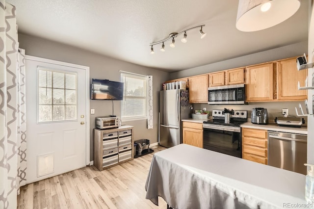 kitchen featuring a textured ceiling, light wood-type flooring, stainless steel appliances, and light brown cabinetry