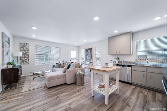 kitchen with light stone counters, dishwasher, sink, and light hardwood / wood-style flooring