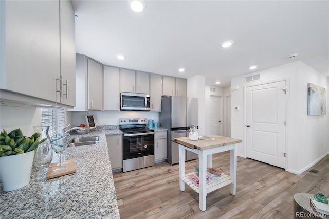 kitchen featuring sink, light hardwood / wood-style flooring, gray cabinets, appliances with stainless steel finishes, and light stone counters