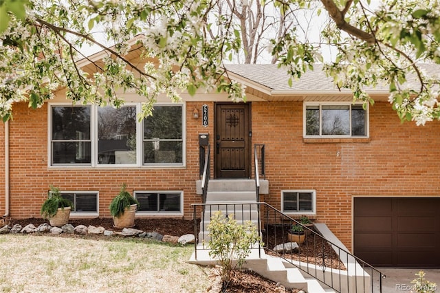 split foyer home with an attached garage, a front yard, and brick siding