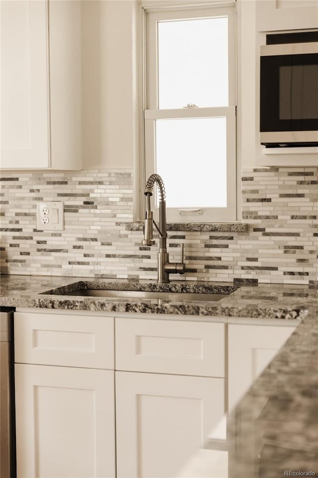 kitchen with a sink, white cabinetry, stainless steel microwave, and backsplash