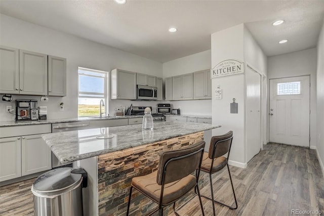 kitchen with a kitchen bar, appliances with stainless steel finishes, light stone countertops, a kitchen island, and sink