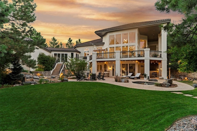 back house at dusk featuring a yard and a patio