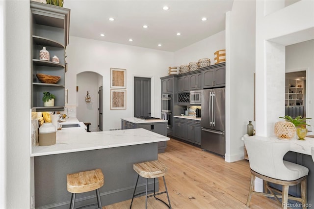 kitchen with a kitchen bar, light wood-type flooring, appliances with stainless steel finishes, kitchen peninsula, and gray cabinets