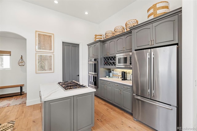 kitchen with light wood-type flooring, light stone counters, a kitchen island, stainless steel appliances, and gray cabinets