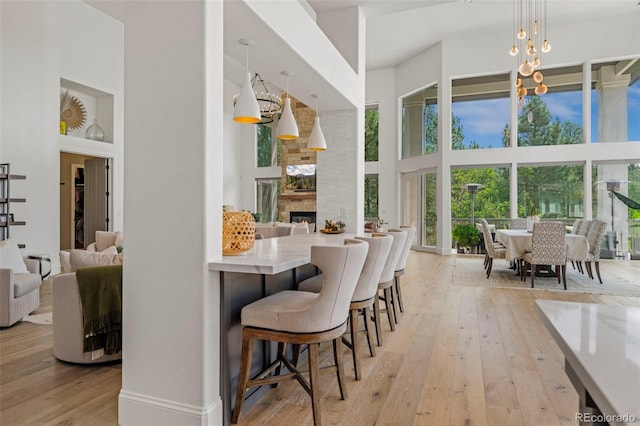 kitchen with a breakfast bar, a high ceiling, a fireplace, light hardwood / wood-style flooring, and hanging light fixtures