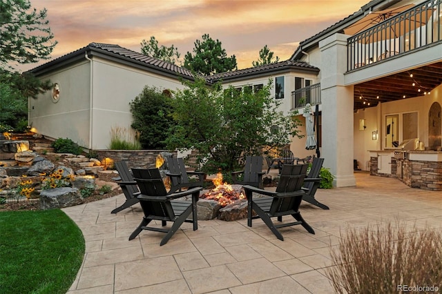 patio terrace at dusk featuring a balcony, an outdoor fire pit, and an outdoor kitchen