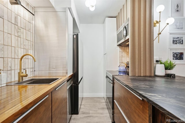 790 N Washington St Unit 407, Denver, CO 80203 - kitchen featuring appliances with stainless steel finishes, butcher block counters, decorative backsplash, and light wood-type flooring