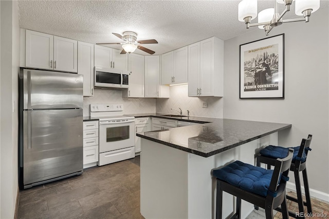 kitchen featuring dark countertops, a sink, white appliances, ceiling fan with notable chandelier, and a peninsula