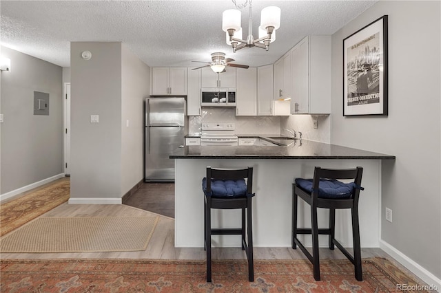 kitchen with white electric range oven, a sink, ceiling fan with notable chandelier, freestanding refrigerator, and wood finished floors