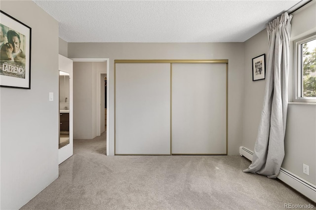 unfurnished bedroom with carpet flooring, a textured ceiling, a baseboard heating unit, and a closet