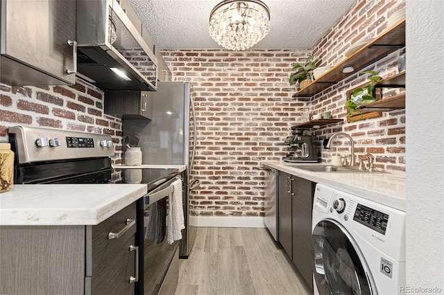 kitchen with brick wall, appliances with stainless steel finishes, washer / clothes dryer, sink, and a textured ceiling