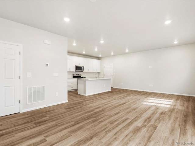 unfurnished living room featuring visible vents, a sink, light wood finished floors, and baseboards