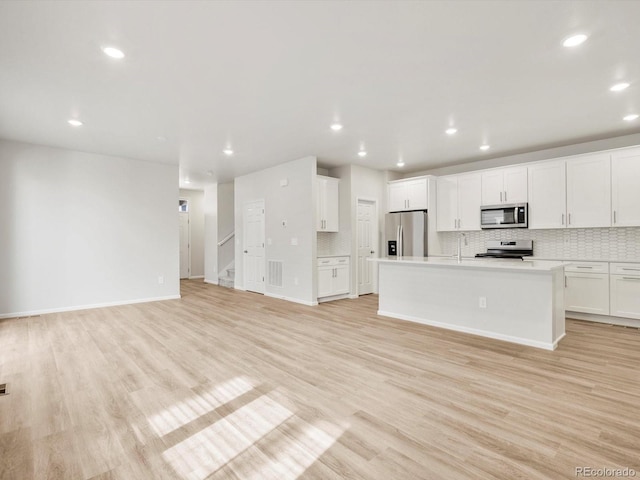kitchen featuring white cabinets, tasteful backsplash, light countertops, stainless steel appliances, and light wood-type flooring